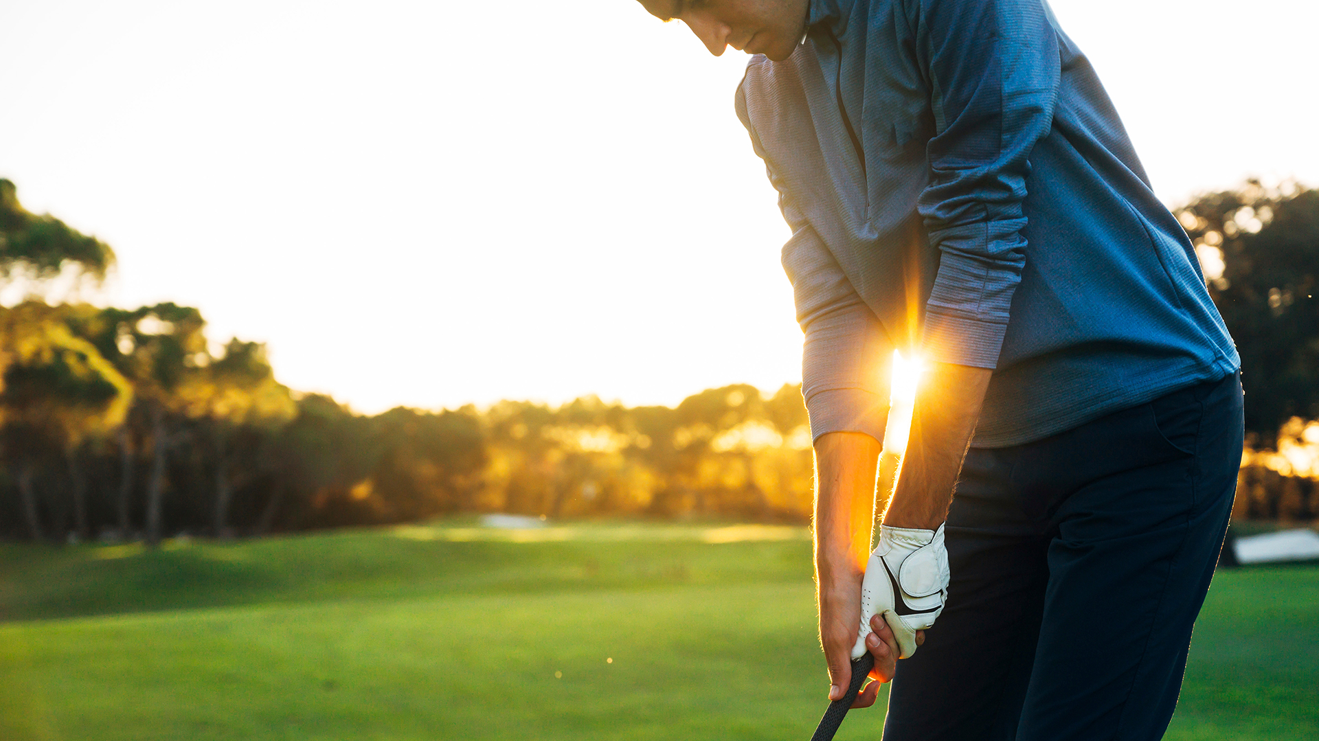 Almost-retired male golf player teeing off golf ball from tee box into the sunset.