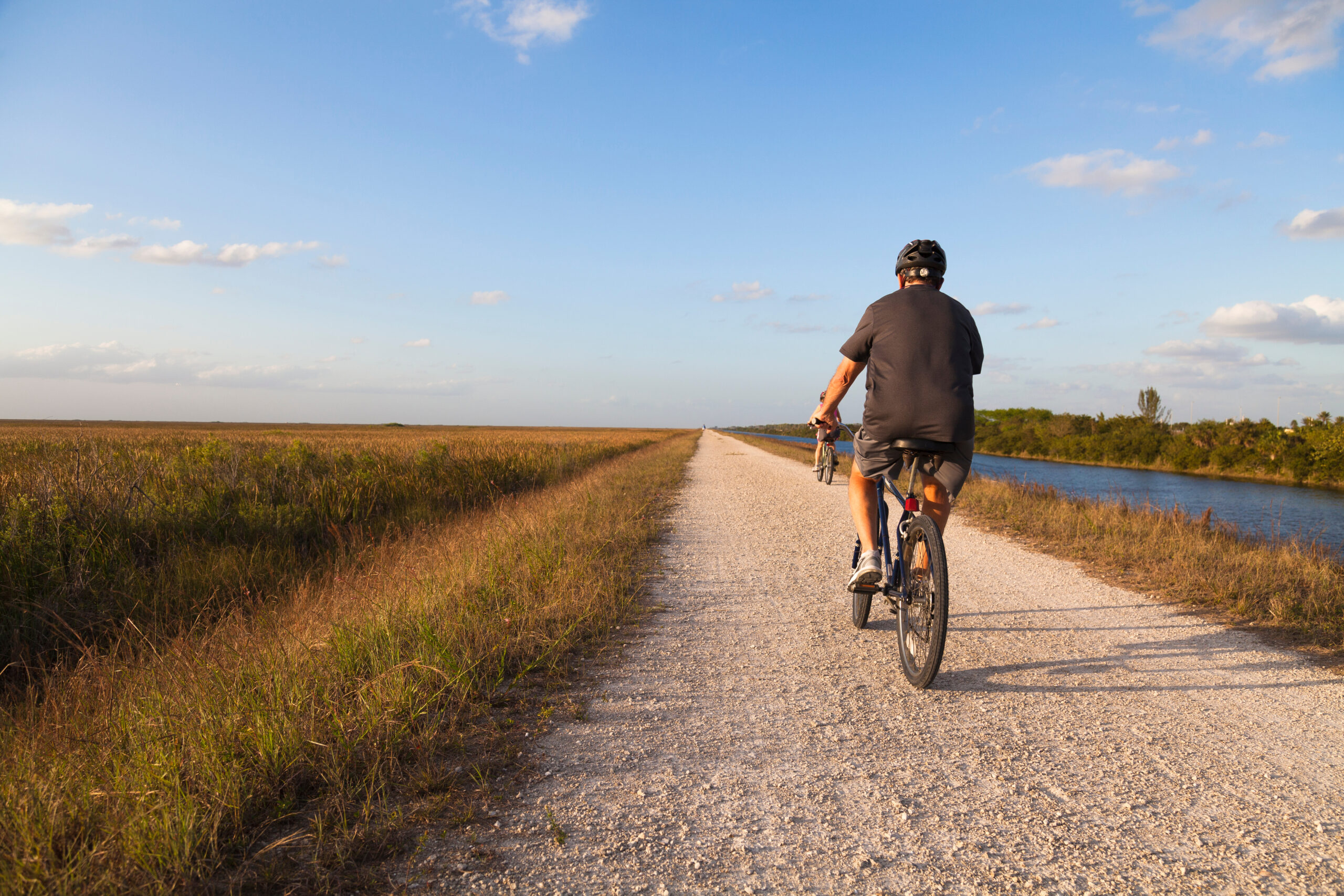 Retired man biking on a path next to a river and plains in the Everglades National Park, Coral Springs, Florida.